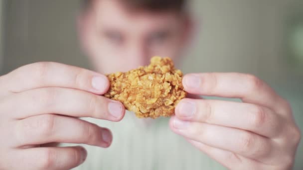 Un hombre hambriento mira a un pollo. Chico retuerce un ala de pollo frito en sus manos — Vídeos de Stock