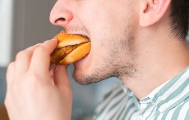 Bir adam abur cubur yer, yakın plan. Adam tavuk burger yiyor.