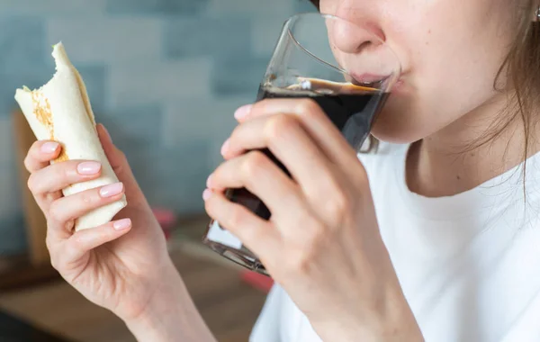 Vrouw drinkt cola en eet kebab. Een mooi meisje bijt een kippenrol van dichtbij. Heerlijk en schadelijk fastfood — Stockfoto