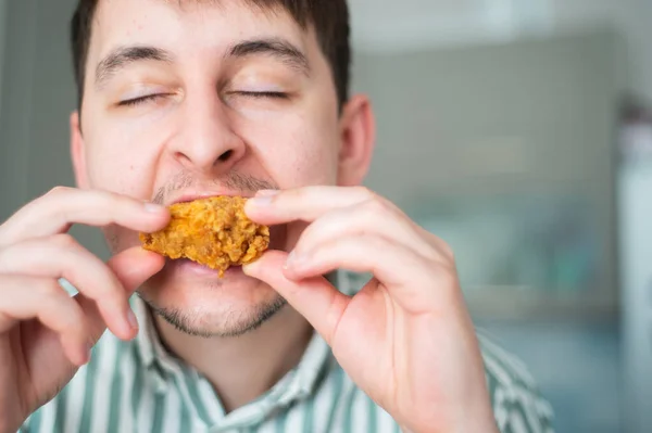 De mens eet pittige kip. Hete kippenvleugels, kerel bijt af pittige kip met gesloten ogen — Stockfoto