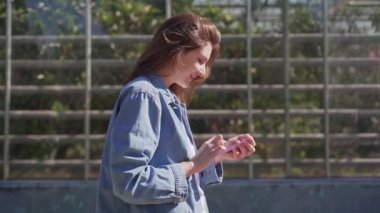 5g telefon. Milenyum genç kadın yeşil bir şehirde yürürken telefonla iletişim kuruyor. Kız geçiyor, telefona bakıyor.