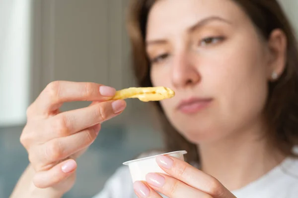 Жінка занурює картоплю фрі у соус. Нездорова швидка їжа — стокове фото