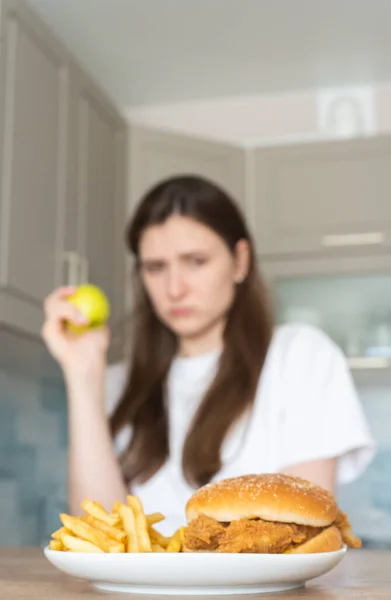 Veganerin isst vor dem Hintergrund ungesunden Fast Food einen Apfel. Die Wahl der richtigen Nahrung — Stockfoto