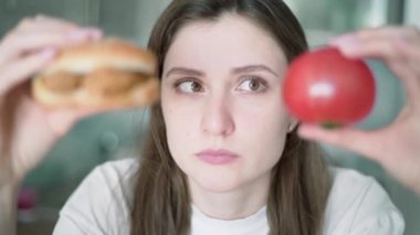 Abur cuburun cazibesi. Kız ne yiyeceğini düşünüyor. Güzel bir kadın elinde domates ve çizburgerle onlara bakıyor.
