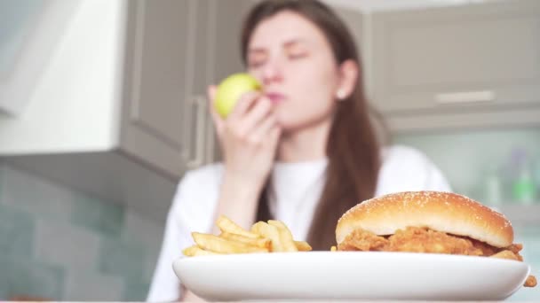 Veganka jí jablko na pozadí nezdravého rychlého občerstvení. Výběr správného jídla — Stock video