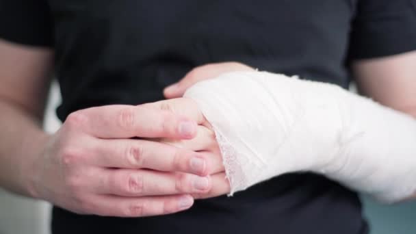 Egy fiatal férfi egészséges keze gipszben masszírozza a törött karját. A sérült kar helyreállítása közeli törést követően — Stock videók
