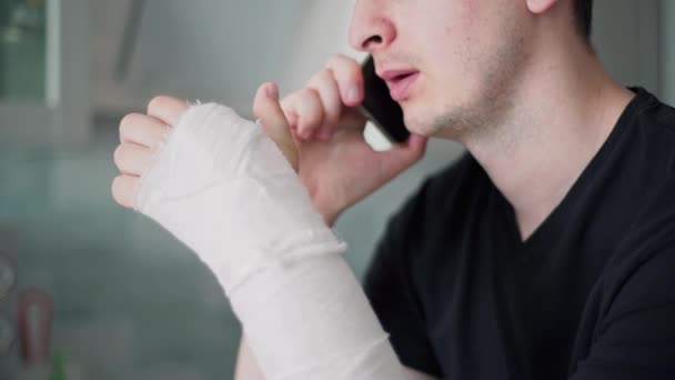 La persona con la mano rota habla por teléfono. Trabajar como autónomo durante una licencia por enfermedad — Vídeos de Stock