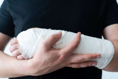 Sağlıklı bir genç adam, yaralı bir kolu bandajla yakın plan çekimde destekler. Bir kırıkta kendini hareket ettirmenin zorluğu.