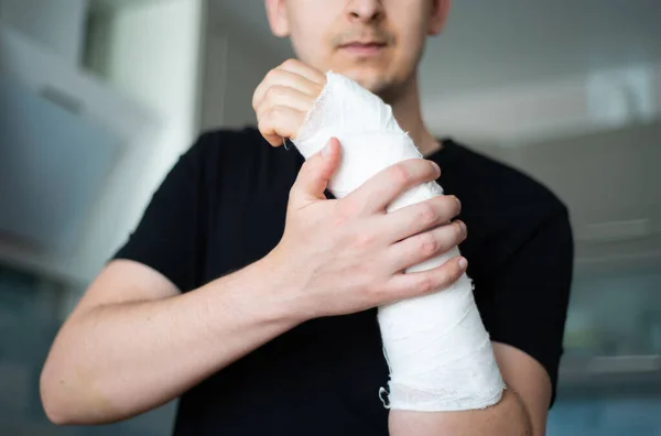 Egy fiatalember úgy ellenőrzi a gipszkötést, hogy hozzáér egy törött karhoz. — Stock Fotó