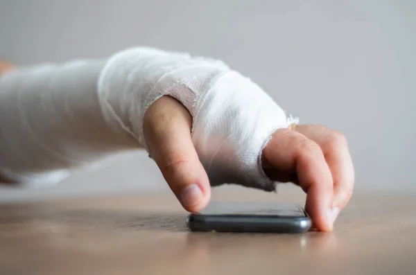 Uma pessoa com uma fractura está a tentar atender o telefone. Desconforto por lesão, dor no braço doente — Fotografia de Stock