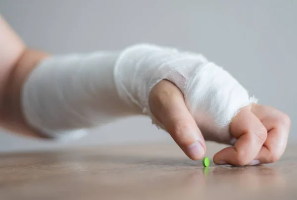 A törött kéz a kötésben megpróbál bevenni egy fájdalomcsillapítót. Stressz és fájdalom sérülés után — Stock Fotó