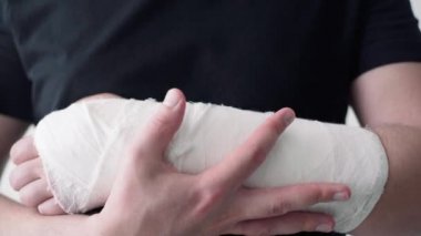 Sağlıklı bir genç adam, yaralı bir kolu bandajla yakın plan çekimde destekler. Bir kırıkta kendini hareket ettirmenin zorluğu.