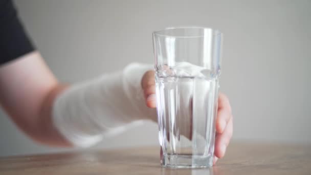 A man with a broken bone tries to take a glass of water. Disability. Bandage on the wrist — Stock Video