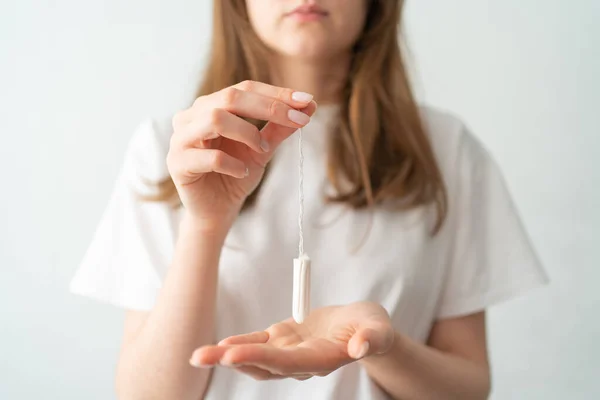 Un tampón en las manos de las mujeres sobre un fondo blanco. Período de menstruación. Protección durante la menstruación —  Fotos de Stock