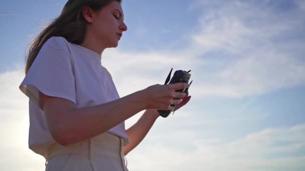 Une belle fille plie un drone et le met sur sa main. gadget technologique dans les mains des femmes au coucher du soleil contre le ciel — Video