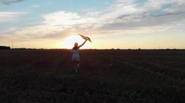 Genç bir kadın güzel bir günbatımında elinde uçurtmayla sahada koşar. Uçurtması olan ince bir kadının silueti.