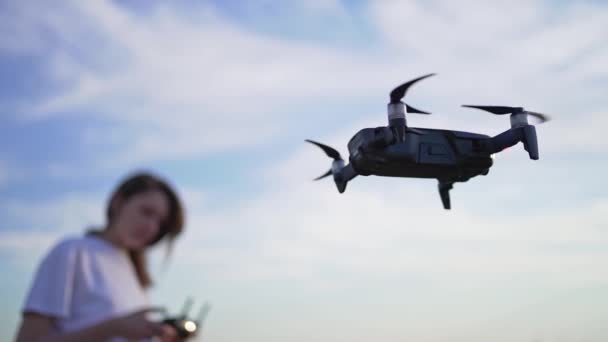 Una mujer controla el vuelo de un dron. El quadcopter flotaba en el aire, el piloto de drones hembra comprueba la configuración del vuelo y mira el dron — Vídeo de stock