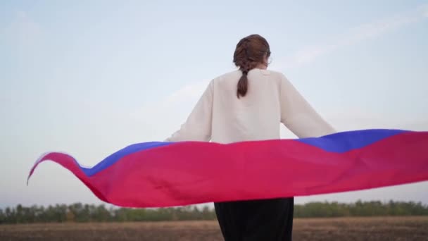 Ρωσική σημαία. Πίσω όψη μιας γυναίκας που περπατάει με μια σημαία στη φύση. Σύμβολο ανεξαρτησίας και πατριωτισμού της Ρωσικής Ομοσπονδίας — Αρχείο Βίντεο