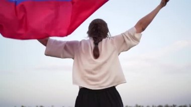 Sıska kadın arkasında Rus bayrağıyla koşuyor, arkadan bakıyor. Rusya Federasyonu bayrağı rüzgarda sallanan bir kadının elinde yavaşça sallanıyor.