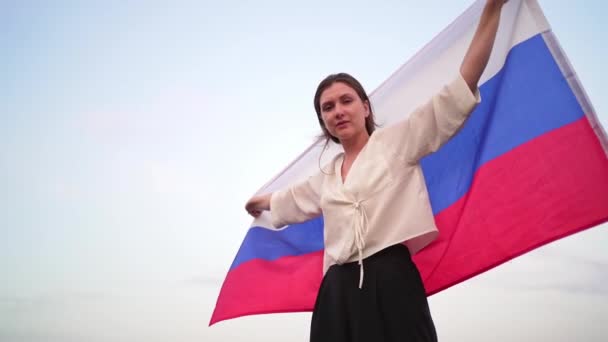 Porträt einer schönen russischen Frau mit einer Flagge bei Sonnenuntergang gegen den Himmel — Stockvideo