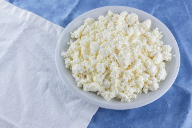 Bir beyaz mavi kumaş arka plan, beyaz bir plaka üzerinde yumuşak peynir, taze ev yapımı peynir beyaz mavi peçeteye süzme peynir. Süt ürünleri vintage tarzı, sağlıklı bir yaşam tarzı. Kopya alanı