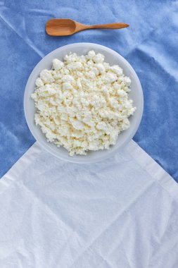 Bir beyaz mavi kumaş arka plan, beyaz bir plaka üzerinde yumuşak peynir, taze ev yapımı peynir beyaz mavi peçeteye süzme peynir. Süt ürünleri vintage tarzı, sağlıklı bir yaşam tarzı. Kopya alanı