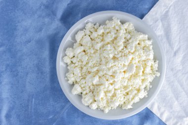 Bir beyaz mavi kumaş arka plan, beyaz bir plaka üzerinde yumuşak peynir, taze ev yapımı peynir beyaz mavi peçeteye süzme peynir. Süt ürünleri vintage tarzı, sağlıklı bir yaşam tarzı. Kopya alanı