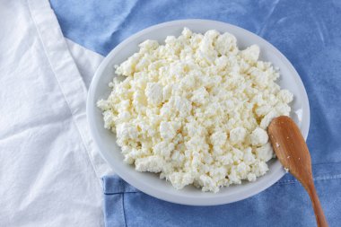 Bir beyaz mavi kumaş arka plan, beyaz bir plaka üzerinde yumuşak peynir, taze ev yapımı peynir beyaz mavi peçeteye süzme peynir. Süt ürünleri vintage tarzı, sağlıklı bir yaşam tarzı. Kopya alanı