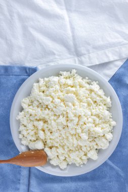 Bir beyaz mavi kumaş arka plan, beyaz bir plaka üzerinde yumuşak peynir, taze ev yapımı peynir beyaz mavi peçeteye süzme peynir. Süt ürünleri vintage tarzı, sağlıklı bir yaşam tarzı. Kopya alanı