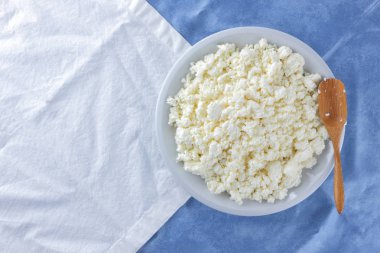 Bir beyaz mavi kumaş arka plan, beyaz bir plaka üzerinde yumuşak peynir, taze ev yapımı peynir beyaz mavi peçeteye süzme peynir. Süt ürünleri vintage tarzı, sağlıklı bir yaşam tarzı. Kopya alanı