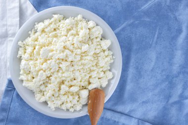 Bir beyaz mavi kumaş arka plan, beyaz bir plaka üzerinde yumuşak peynir, taze ev yapımı peynir beyaz mavi peçeteye süzme peynir. Süt ürünleri vintage tarzı, sağlıklı bir yaşam tarzı. Kopya alanı