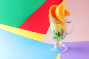 Bir bardak meyve kokteyli tropikal meyve parçaları. Portakal, kivi küpleri, dilimlenmiş dilim ananas bir cam kase. Arka plan çok renkli pop sanat