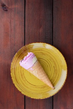 Sarı pembe dondurmalı çikolata gözleme Kupası'nda. Koyu ahşap arka plan dondurma. Soğuk süt tatlı sarı bir plaka üzerinde. Minimalizm tarzı soğuk tatlı yaz