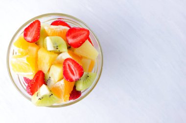 Ananas, kivi, portakal, çilek meyve salatası. Çok renkli dilimlenmiş meyve şeffaf bir tabak içinde. Beyaz bir arka plan üzerinde vejetaryen yemek. Kopya alanı.
