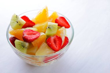 Ananas, kivi, portakal, çilek meyve salatası. Çok renkli dilimlenmiş meyve şeffaf bir tabak içinde. Beyaz bir arka plan üzerinde vejetaryen yemek. Kopya alanı.