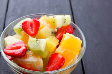 Ananas, kivi, portakal, çilek meyve salatası. Çok renkli dilimlenmiş meyve şeffaf bir tabak içinde. Siyah ahşap zemin Vejetaryen yiyecekler. Kopya alanı