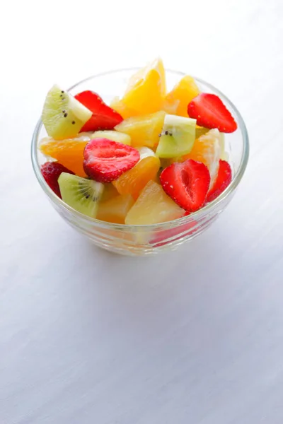 Fruit salad from pineapple, kiwi, orange, strawberry. Multicolored sliced fruit in a transparent dish. Vegetarian meal on a white background. Copy space.