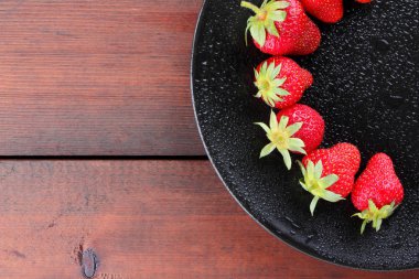 Çilek siyah plaka üstten görünüm üzerinde kırmızı bir ahşap arka plan üzerinde koyu ahşap kurullarında vejetaryen yemek taze çilek çilek
