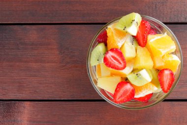 Ananas, kivi, portakal, çilek meyve salatası. Çok renkli dilimlenmiş meyve şeffaf bir tabak içinde. Vejetaryen yiyecekler ahşap arka plan üzerinde. Narenciye Asya mutfağı