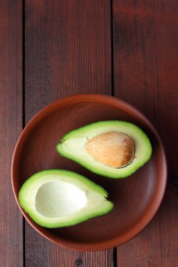 Ahşap arka plan üzerinde avokado, iki yarım avokado kil tabakta, retro tarzı, vejetaryen yemek, kopya alanı, tropikal meyve görünümü top