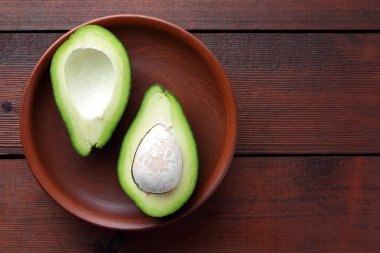 Ahşap arka plan üzerinde avokado, iki yarım avokado kil tabakta, retro tarzı, vejetaryen yemek, kopya alanı, tropikal meyve görünümü top