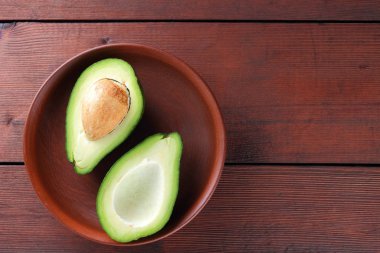 Ahşap arka plan üzerinde avokado, iki yarım avokado kil tabakta, retro tarzı, vejetaryen yemek, kopya alanı, tropikal meyve görünümü top