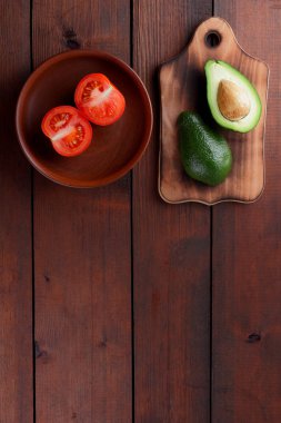 Avokado bir eski ahşap tahta, yarıya avokado ve ahşap arka plan üzerinde domates, yeşil tropikal meyve üst görüntülemek, vintage bir arka plan kopya alanı üzerinde kırmızı ve yeşil sebzeler