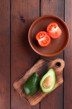 Avokado bir eski ahşap tahta, yarıya avokado ve ahşap arka plan üzerinde domates, yeşil tropikal meyve üst görüntülemek, vintage bir arka plan kopya alanı üzerinde kırmızı ve yeşil sebzeler