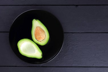 Siyah bir plaka üzerinde avokado, avokado bir siyah ahşap arka plan, yeşil tropikal meyve üst yarıyı da görüntülemek, minimalist tarzda egzotik meyve