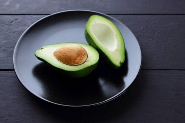 Siyah bir plaka üzerinde avokado, avokado bir siyah ahşap arka plan, yeşil tropikal meyve üst yarıyı da görüntülemek, minimalist tarzda egzotik meyve