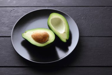 Siyah bir plaka üzerinde avokado, avokado bir siyah ahşap arka plan, yeşil tropikal meyve üst yarıyı da görüntülemek, minimalist tarzda egzotik meyve