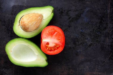 Avokado ve karanlık bir metal yüzeyi domates Yarım avokado ve yaşlı bir metal arka plan, kırmızı ve yeşil sebze yukarıdan, minimalist tarzda egzotik meyve domates