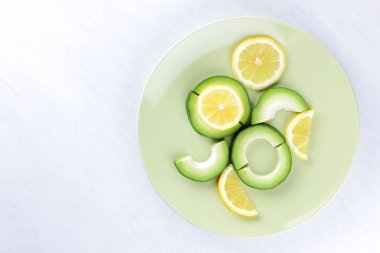 Avokado ve limon bir yeşil plaka, beyaz arka plan, Vejetaryen gıda, yararlı doğal gıda, tropik meyveler avokado kahvaltı için dilimlenmiş, kopyalama alanı