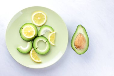 Avokado ve limon bir yeşil plaka, beyaz arka plan, Vejetaryen gıda, yararlı doğal gıda, tropik meyveler avokado kahvaltı için dilimlenmiş, kopyalama alanı